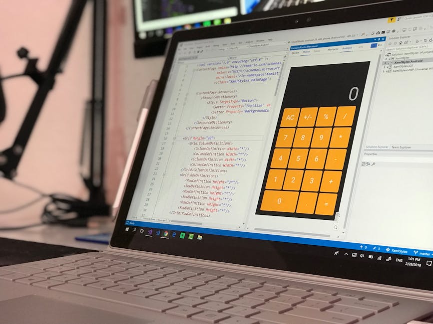 A close-up view of a laptop computer displaying a software development environment with lines of code in various colors and a large, orange calculator interface on the screen. The laptop is positioned
