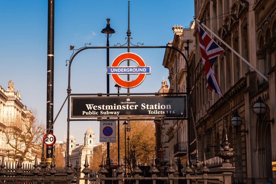 A busy scene outside Westminster Underground Station in London, featuring a black metal staircase leading down to the subway entrance, which is topped by a classic Underground sign with a red circle a